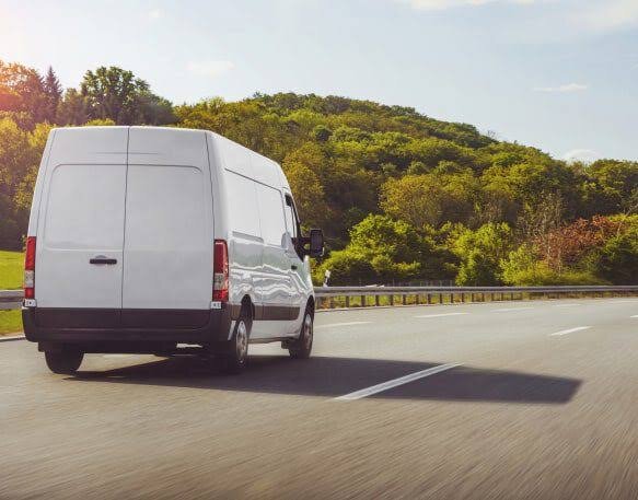 Bijeli teretni kombi na cesti uz zelenilo